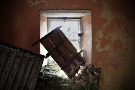 A partly boarded up window in the entrance porch